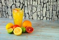 A tall glass of citrus juice with a straw and slices of fruit, stands on a wooden table, next to sliced orange, lemon, lime and Royalty Free Stock Photo