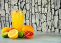 A tall glass of citrus juice with a straw and slices of fruit, stands on a wooden table, next to sliced orange, lemon, lime and Royalty Free Stock Photo