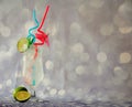 Tall glass of clear fruit nectar with ice and straws, decorated with a slice of lime on a gray glittering background