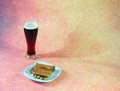 Tall glass of dark beer with foam and a plate with fresh wheat croutons on a brown abstract background Royalty Free Stock Photo