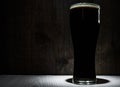 Tall glass of dark beer over a dark wooden background
