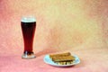 Tall glass of dark beer with white foam and a plate with fresh wheat croutons on a brown abstract background Royalty Free Stock Photo