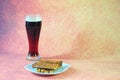 Tall glass of dark beer with white foam and a plate with fresh wheat croutons on a brown background Royalty Free Stock Photo