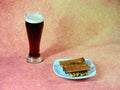 A tall glass of dark beer with white foam and a plate with fresh wheat croutons on a brown background Royalty Free Stock Photo