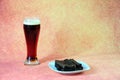 A tall glass of dark beer with white foam and a plate with fresh wheat croutons on a brown background Royalty Free Stock Photo