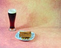 A tall glass of dark beer with white foam and a plate with wheat croutons