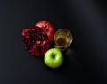 A tall glass of freshly squeezed fruit juice on a black background, next to a broken pomegranate fruit with seeds and a ripe green Royalty Free Stock Photo