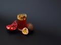 A tall glass of juice with seeds on a black background, next to a broken pomegranate fruit and pieces of ripe passion fruit Royalty Free Stock Photo