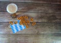 Tall glass of light beer with foam on a traditional napkin in a handful of pretzels with salt on a wooden table