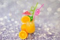 A tall glass of orange juice with ice and a slice of lemon with straws and an umbrella, near exotic fruits on a gray abstract Royalty Free Stock Photo