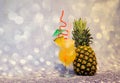 A tall glass of pineapple juice with ice and a slice of tropical fruit next to a ripe pineapple stand against a gray shiny Royalty Free Stock Photo