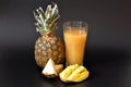 A tall glass of pineapple juice with mango and pieces of ripe fruit on a black background Royalty Free Stock Photo