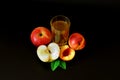 A tall glass with red apple and peach juice on a black background, next to pieces of ripe fruit Royalty Free Stock Photo