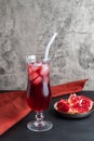 A tall glass of red juice with ice and straws on a gray background, next to a ripe pomegranate fruit, underlaid with a cloth Royalty Free Stock Photo