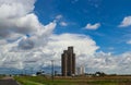 Tall grain elevators in the midwestern United States sorrounded by trucks and equipment and powerlines beside a highway all under Royalty Free Stock Photo