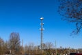 A tall gray radio tower surrounded by brown and bare winter trees with blue sky in Douglasville