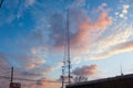 A tall gray radio tower surrounded by brown and bare winter trees with blue sky and powerful clouds at sunset