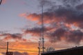 A tall gray radio tower surrounded by brown and bare winter trees with blue sky and powerful clouds at sunset