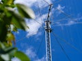 Tall ham radio antenna against a blue cloudy sky behind green leaves Royalty Free Stock Photo