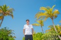 Tall handsome man wearing white t-shirt and black shorts standing at tropical sandy beach at island luxury resort Royalty Free Stock Photo