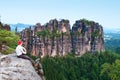 Tall man with red baseball cap sit on cliff and watch to mountains. Dark silhouette of rocks. Royalty Free Stock Photo