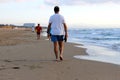 A tall man walking along the sea shore of a large beach