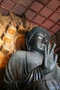 Large bronze Buddha statue with right hand raised in wooden temple with gold backdrop Royalty Free Stock Photo