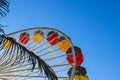 A tall metal Ferris wheel with colorful cars around the wheel on with blue sky the Santa Monica Pier
