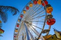 A tall metal Ferris wheel with colorful cars around the wheel on with blue sky the Santa Monica Pier