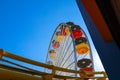 A tall metal Ferris wheel with colorful cars around the wheel on with a yellow rollercoaster rail and blue sky