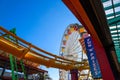 A tall metal Ferris wheel with colorful cars around the wheel on with a yellow rollercoaster rail and blue sky