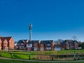 A tall mobile phone mast next to modern residential housing with a grassed area and pond in the foreground.. Royalty Free Stock Photo