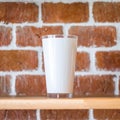 Tall mug on vintage brick wall background. Wooden display shelf for showing transparent drink cup in grunge concept. Brickwork