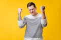 Tall muscular young man in a striped shirt making sucsess gesture over yellow Royalty Free Stock Photo