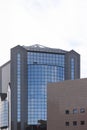 A tall office building with blue windows and sky reflecting on it. A clear white sky is above the building. A darker house is Royalty Free Stock Photo