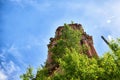 A tall old stone bell tower made of red brick against a blue sky with white clouds and green trees around. Partially Royalty Free Stock Photo