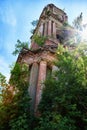 A tall old stone bell tower made of red brick against a blue sky with white clouds and green trees around. Partially Royalty Free Stock Photo