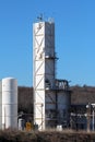 Tall old white rectangle storage silo rising above row of brand new storage silos at oil refinery complex Royalty Free Stock Photo