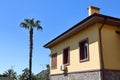 A tall palm tree and a yellow house with a chimney against a blue sky in Alanya, Turkey, April 2021 Royalty Free Stock Photo