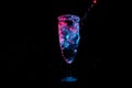 Party glass overflowing with splashing liquid shining in blue and red light isolated on a black background Royalty Free Stock Photo