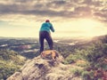 Tall photographer with baseball cap and tripod with camera in hands stand on rocky view point and watching down to deep misty