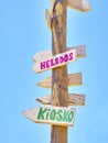 Tall post with colored wooden signboards pointing to various destinations and a beach services in Spanish