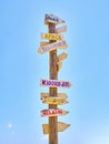 Tall post with colored wooden signboards pointing to various destinations and a beach services in Spanish