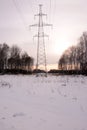 A tall power line pole stands in a field covered with snow at sunset Royalty Free Stock Photo