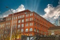 A tall red brick building with some boarded up windows on the street with a blue sky and powerful clouds Royalty Free Stock Photo