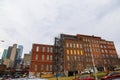 Tall red brick buildings with boarded up and broken windows with bare winter trees in front on the riverfront with cloudy gray sky