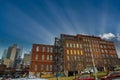 Tall red brick buildings with boarded up and broken windows with bare winter trees in front on the riverfront with cloudy gray sky