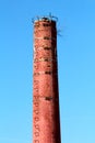 Tall red brick industrial chimney with metal lightning rod and steps without safety wire at abandoned industrial complex