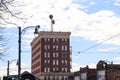 A tall red brick office buildings with a radio tower on top surrounded by other buildings and tall curved lamp posts