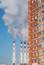 Tall residential red building and smoking red and white chimneys of a heating plant, urbanism Royalty Free Stock Photo